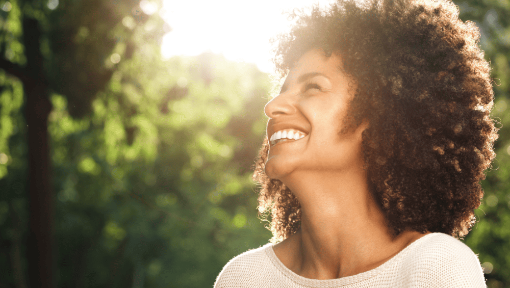 Como Ter Um Glow Up - Confiança é o ponto final - foto de uma mulher sorridente em meio a natureza demonstrando a confiança.