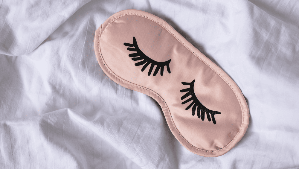 Como Ter Um Glow Up - Durma melhor - mascara que coloca nos olhos para dormir, que veda luz, em cima de um lençol de seda para representar uma boa noite de sono.