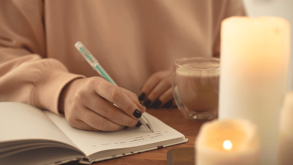 Frases para Aumentar Autoestima - Mensagens de Autoestima e Reflexao, mulher escrevendo em seu diario, café com leite na imagem e uma vela.