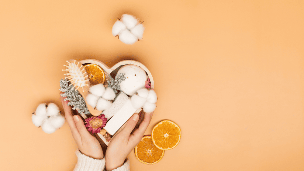 Quais são os 4 tipos de autocuidado - O que significa autocuidado - imagem de um pote em formato de coração com alguns itens de autocuidado, como escova, sabonete, escova de cabelo, com algumas rodelas de laranja ao redor para demonstrar suavidade.