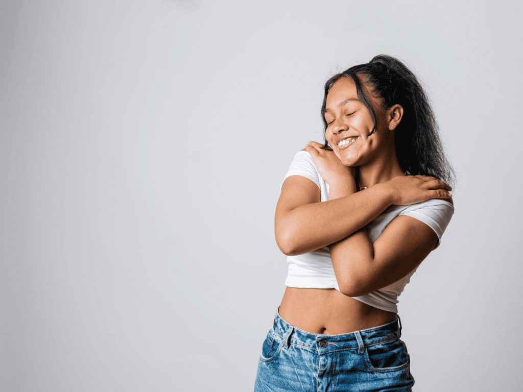 O Que Quer Dizer a Expressão Glow Up - Trabalhe sua autoestima O Que Quer Dizer a Expressão Glow Up - Trabalhe sua autoestima - imagem de uma mulher se abraçando e sorrindo feliz