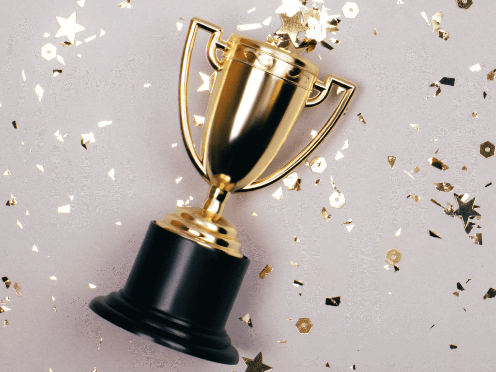 Foto de um troféu dourado em um fundo claro, cercado por confetes e estrelas brilhantes. Simboliza a vitória e os 10 melhores apps para organizar a rotina, representando a excelência e a solução definitiva.