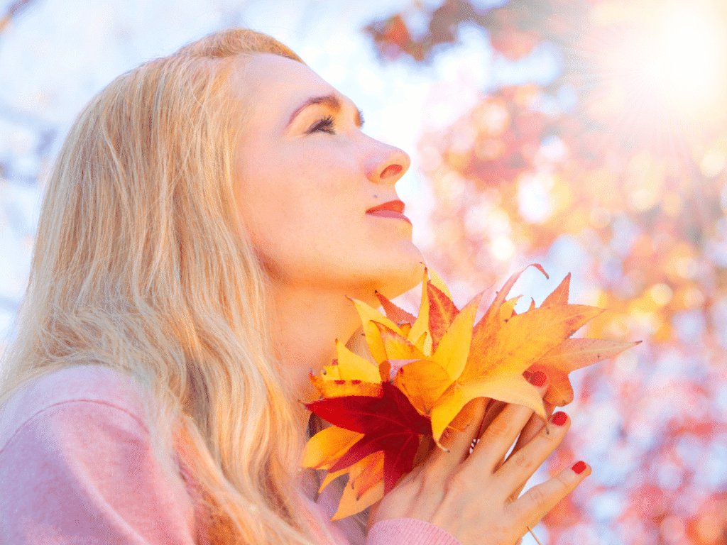 Como Exercitar a Gratidão Diariamente  - Gratidão Pela Sua Jornada Conectando o Bem-Estar - imagem de uma mulher na natureza segurando algumas folhas secas de outono passando uma sensação de libertação, cura, bem estar.