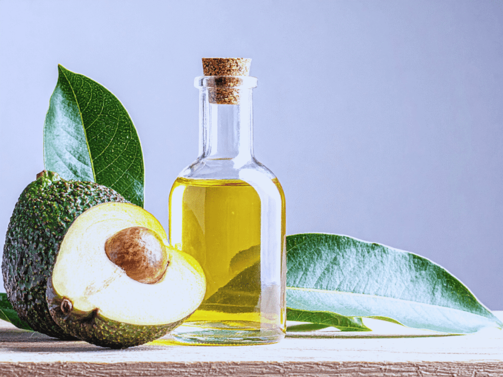 Óleos para Umectação Capilar - Óleo de Abacate Óleos para Umectação Capilar - Óleo de Abacate - imagem com fundo azul, com o abacate em cima de uma madeira, e seu fraco junto com óleo de abacate.